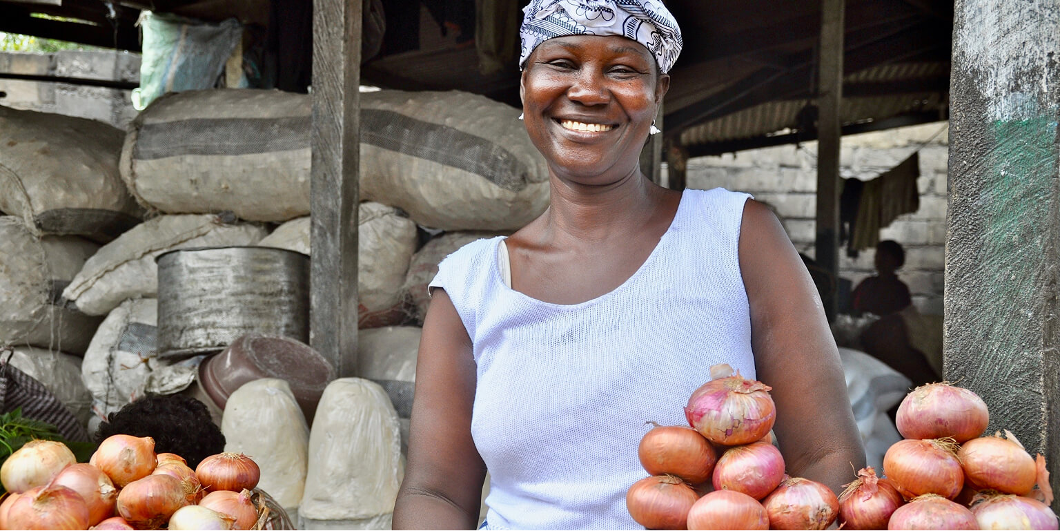 Woman selling onions smiling at the camera.