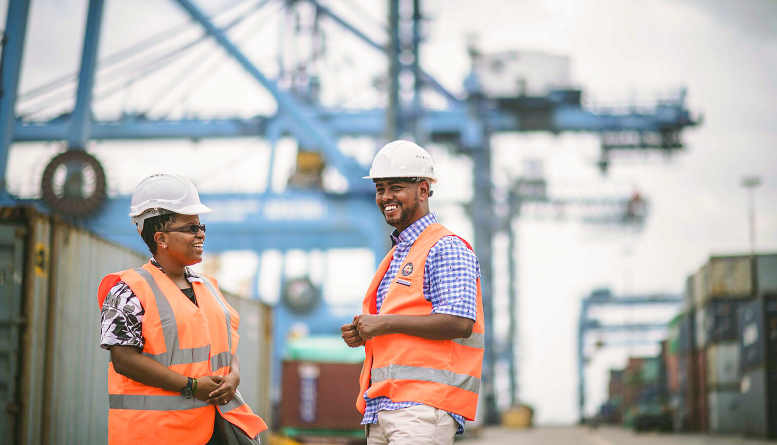 Two workers talking with cranes in the background.