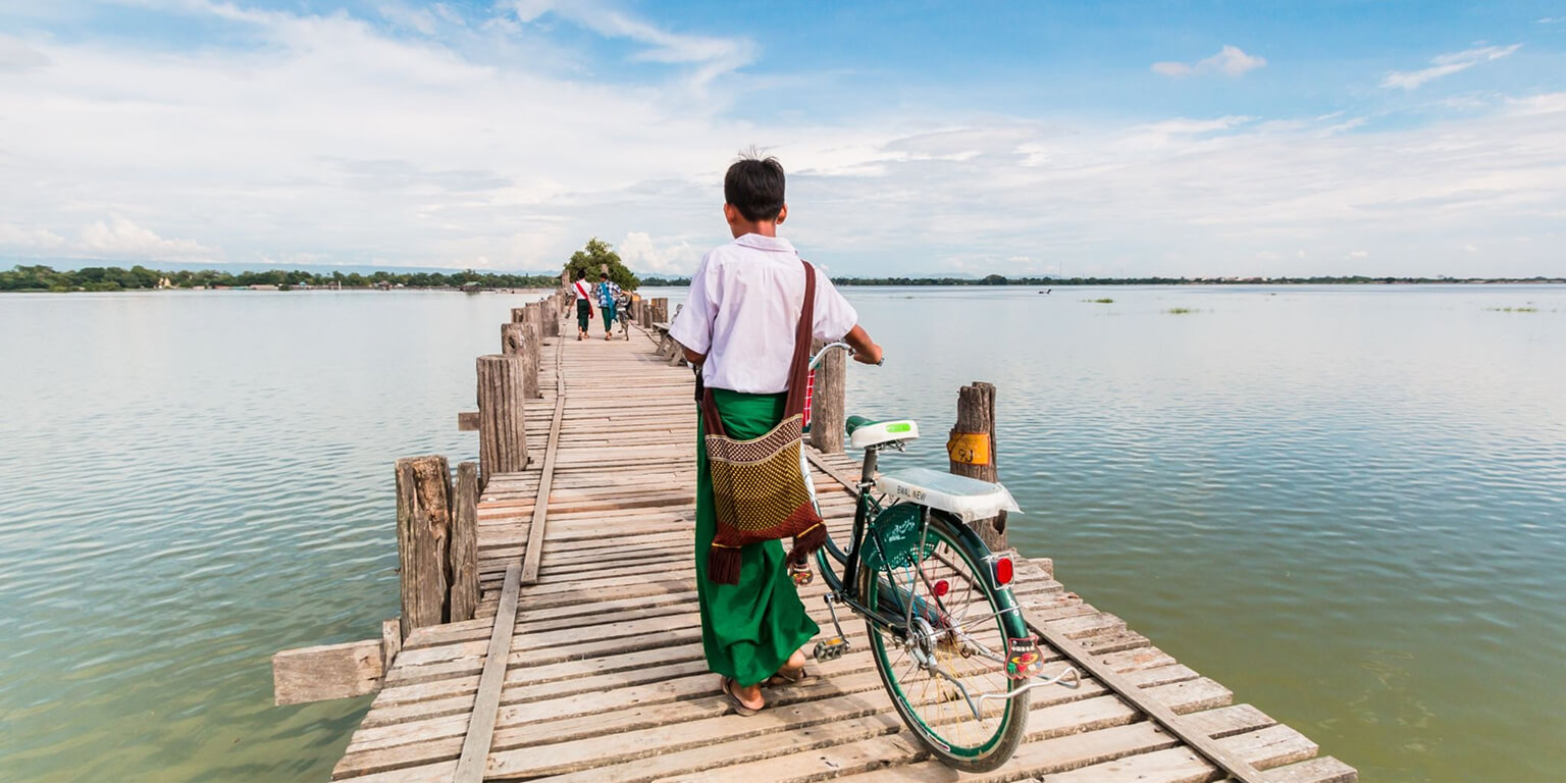 Man with a bicycle walks along wooden bridge in Myanmar