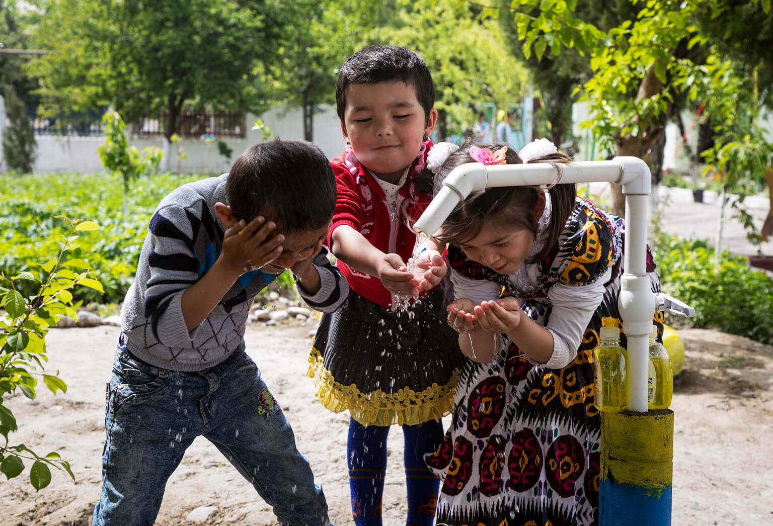 Kids playing and washing their hands under a water tap.